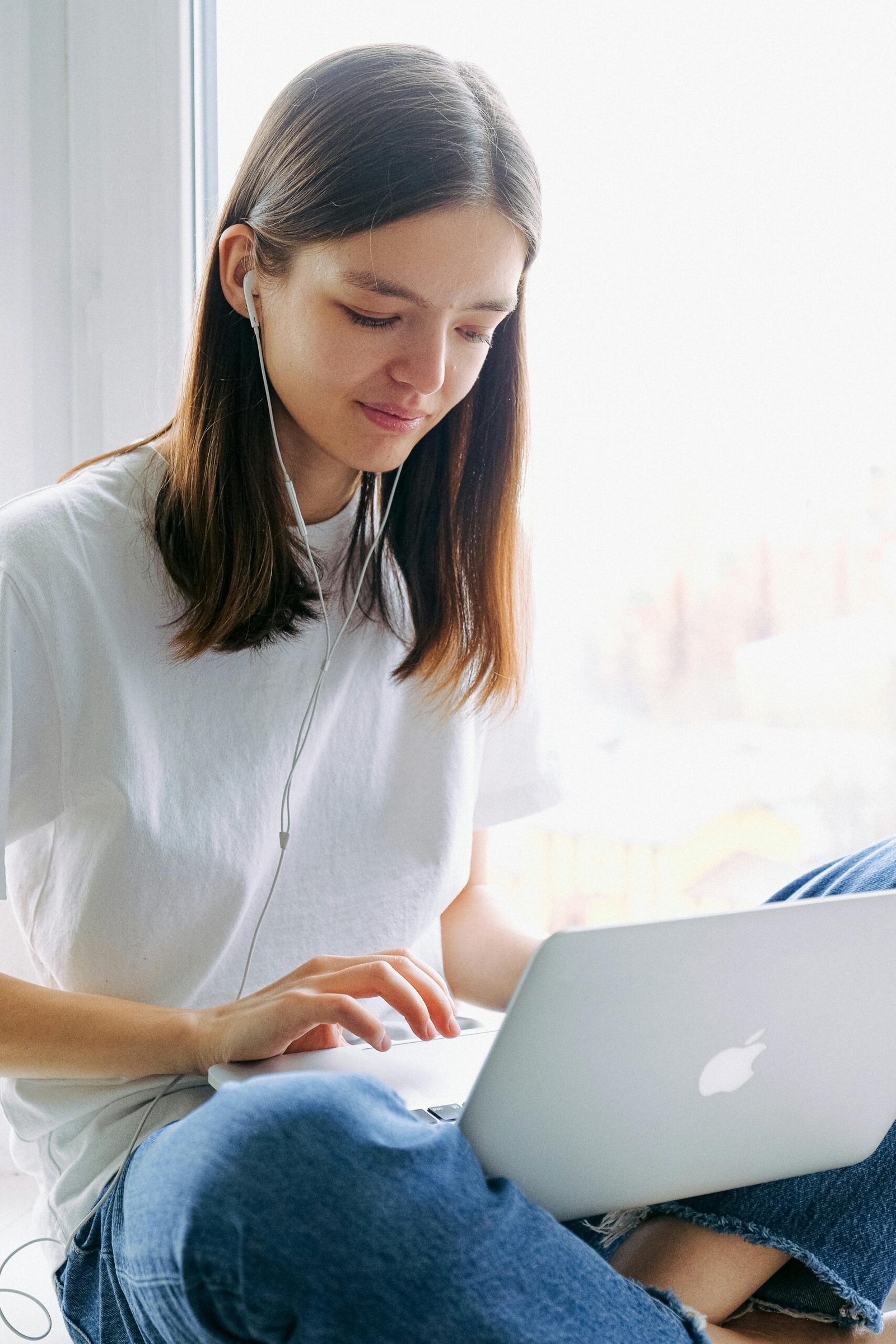 Young woman sitting indoors using her laptop and earphones for remote work.